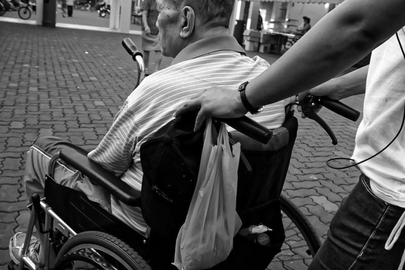 Elderly man in wheelchair pushed by carer