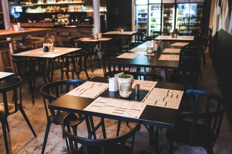 an empty restaurant with assorted black tables and chairs 