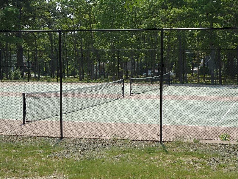 Outdoor tennis court seen through a fence.