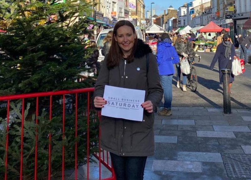 Photo of Vicky next to Christmas tree on Deptford High Street holding sign which reads: "Small Business Saturday"