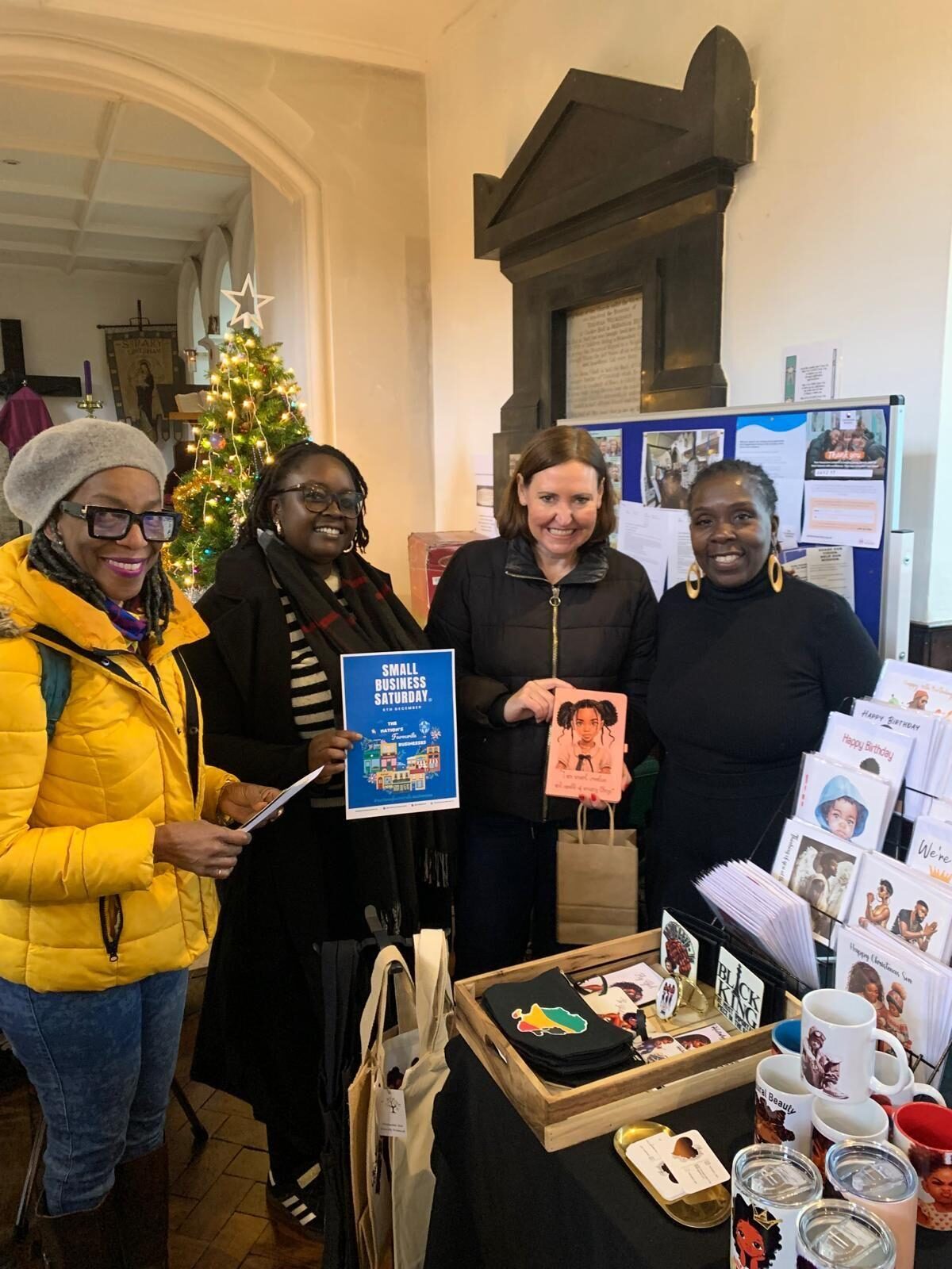 Council Candidates Collet and Ayesha (left) and Vicky (centre) stood smiling with a small business owner and her market stall. 